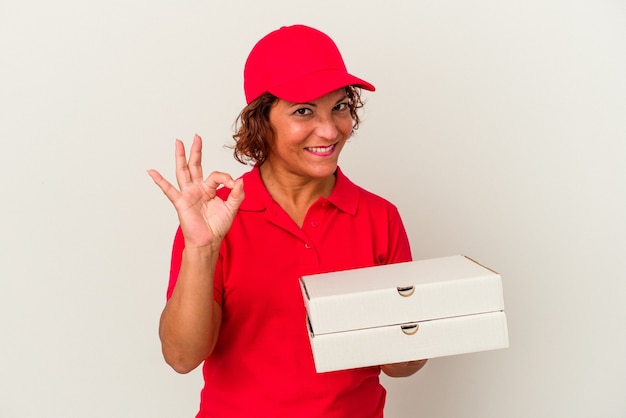 Middle age delivery woman taking pizzas isolated on white background cheerful and confident showing ok gesture.