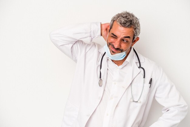 Middle age doctor man wearing a mask for virus isolated on white background touching back of head thinking and making a choice