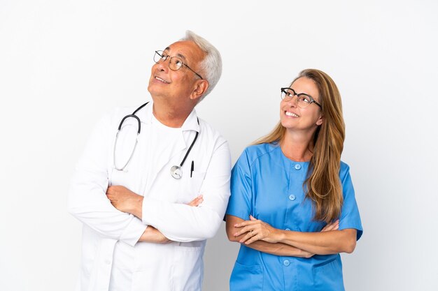 Middle age doctor and nurse isolated on white background looking up while smiling