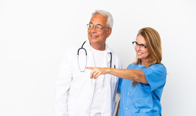 Middle age doctor and nurse isolated on white background pointing to the side to present a product