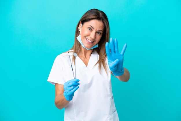 Женщина-врач средних лет, изолированная на синем фоне, счастливая и считая четыре пальцами