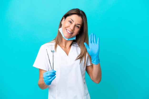 Middle age doctor woman isolated on blue background saluting with hand with happy expression