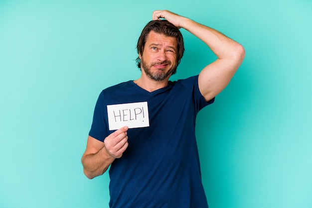 Middle age dutch man holding a help placard isolated on blue background being shocked, she has remembered important meeting.