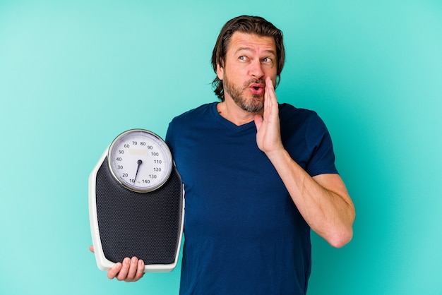 Голландский мужчина средних лет, держащий весы на синей стене, говорит секретные горячие новости о торможении и смотрит в сторону