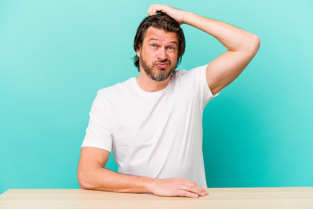 Middle age dutch man sitting isolated on blue background being shocked, she has remembered important meeting.