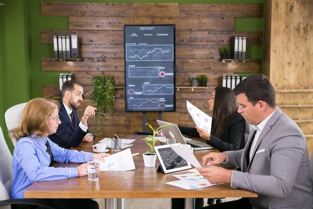 Middle age executive woman having a meeting with her young colleagues in the conference room. Charts on tv screen.