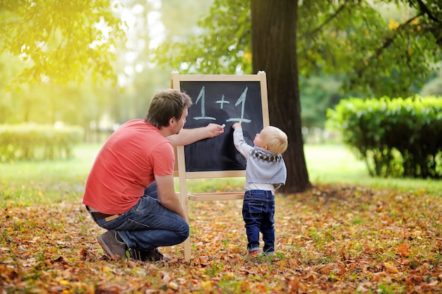 Middle age father and his toddler son at blackboard practicing mathematics