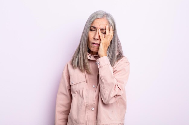 Donna di mezza età con i capelli grigi che si sente annoiata, frustrata e assonnata dopo un compito noioso, noioso e noioso, tenendo il viso con la mano