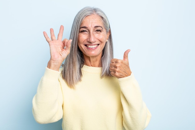 Middle age gray hair woman feeling happy amazed satisfied and surprised showing okay and thumbs up gestures smiling