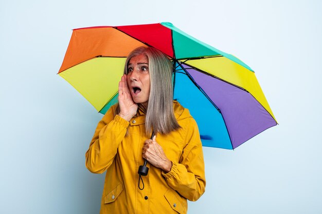 幸せ、興奮、驚きを感じている中年の白髪の女性。傘と雨の概念