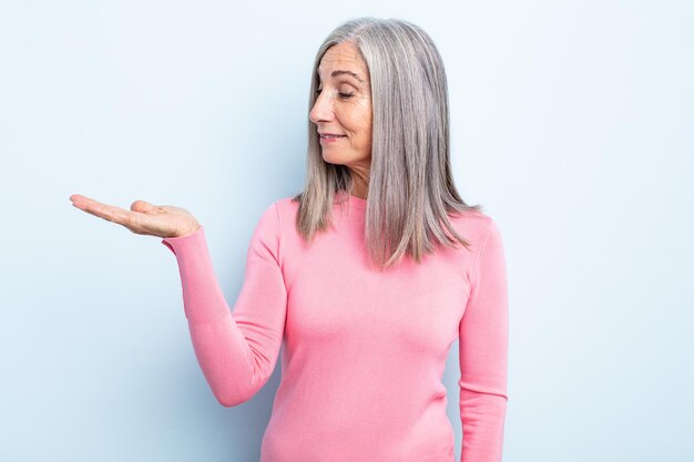 Middle age gray hair woman feeling happy and smiling casually, looking to an object or concept held on the hand on the side