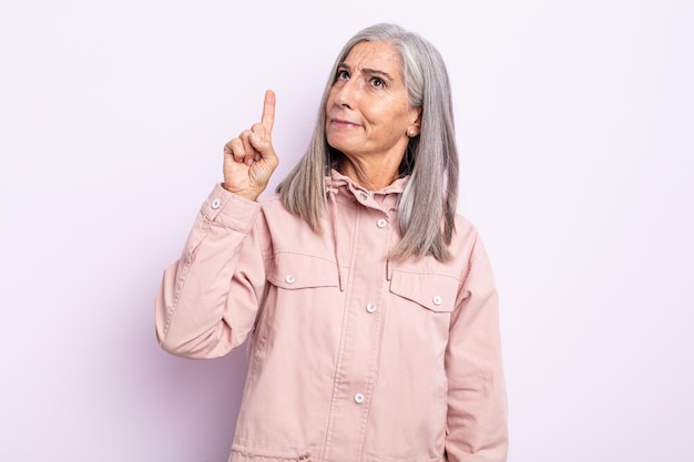 Middle age gray hair woman feeling like a genius holding finger proudly up in the air after realizing a great idea, saying eureka