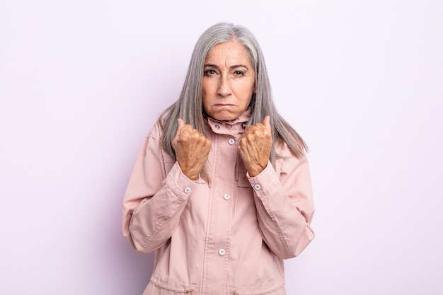 Middle age gray hair woman looking confident, angry, strong and aggressive, with fists ready to fight in boxing position