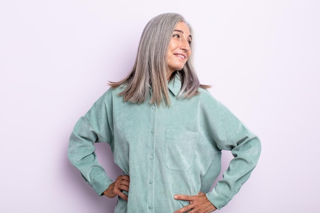 Middle age gray hair woman looking happy, cheerful and confident, smiling proudly and looking to side with both hands on hips