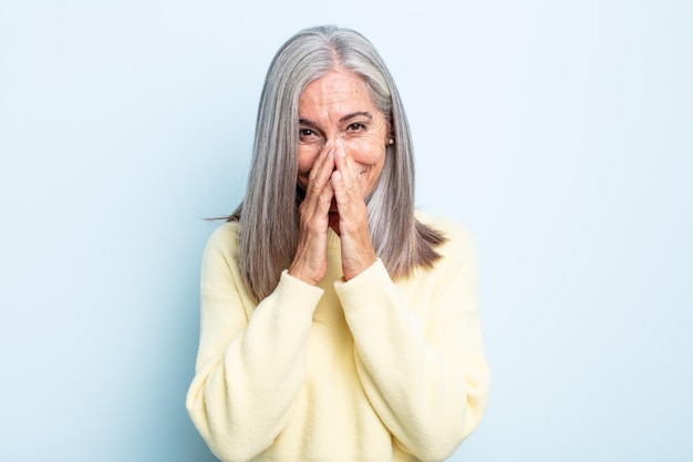 Donna dai capelli grigi di mezza età che sembra felice, allegra, fortunata e sorpresa che copre la bocca con entrambe le mani