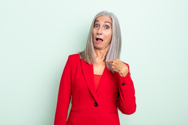 Middle age gray hair woman looking shocked and surprised with mouth wide open, pointing to self. senior businesswoman concept