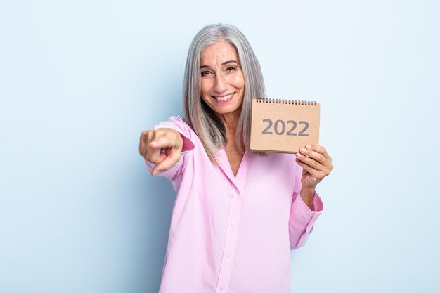Donna di capelli grigi di mezza età che punta alla telecamera scegliendo te. concetto di calendario 2022