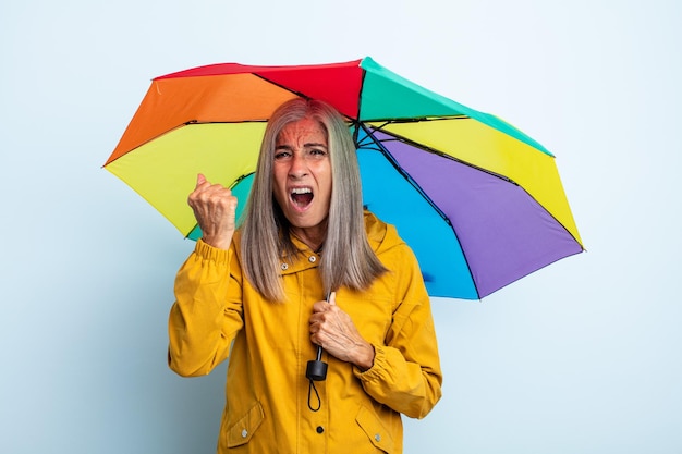 Donna dai capelli grigi di mezza età che grida in modo aggressivo con un'espressione arrabbiata. concetto di ombrello e pioggia