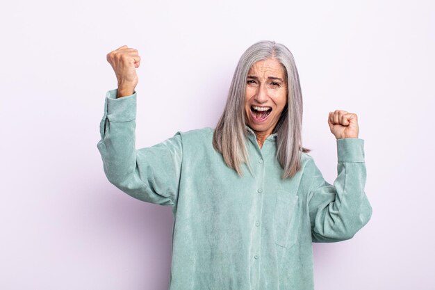 Middle age gray hair woman shouting triumphantly, looking like excited, happy and surprised winner, celebrating