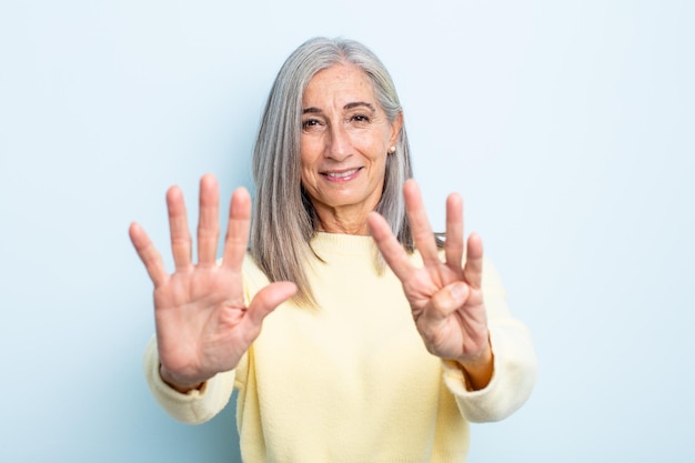 Donna di mezza età con i capelli grigi sorridente e dall'aspetto amichevole, mostrando il numero nove o nono con la mano in avanti, conto alla rovescia