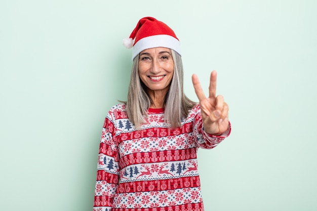 중년의 회색 머리 여성은 미소를 짓고 친절해 보이며 2번을 보여줍니다. 크리스마스 컨셉