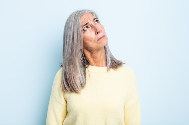 Foto donna di mezza età con i capelli grigi con un'espressione preoccupata, confusa, senza tracce, guardando in alto per copiare lo spazio, dubitando