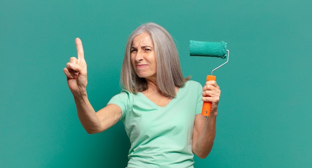 Donna di mezza età con i capelli grigi con un rullo di vernice che decora la sua parete