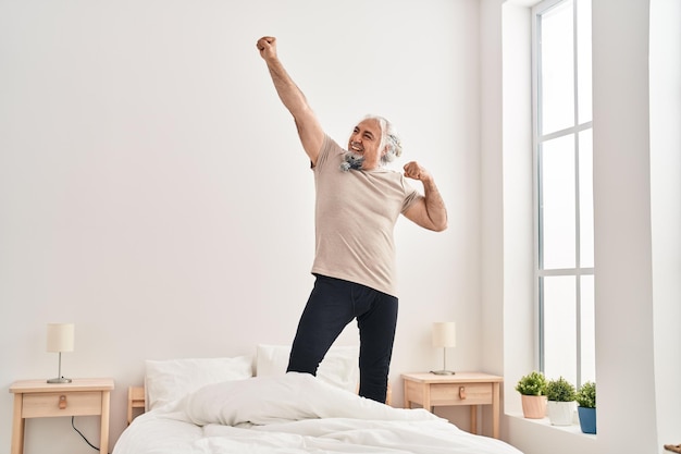 Middle age grey-haired man smiling confident dancing on bed at bedroom