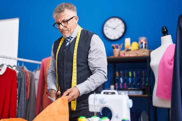 Middle age grey-haired man tailor cutting cloth at clothing factory