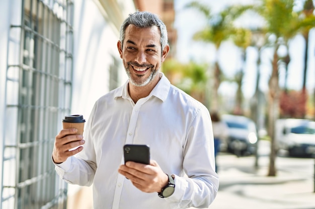 街でコーヒーを飲みながらスマートフォンを使う中年の白髪の男性。