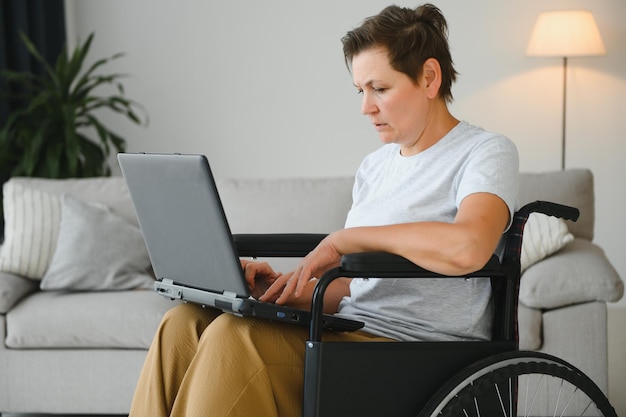 Middle age greyhaired disabled woman having video call sitting on wheelchair at home