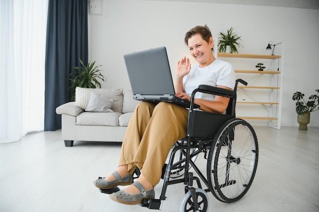 Middle age greyhaired disabled woman having video call sitting on wheelchair at home