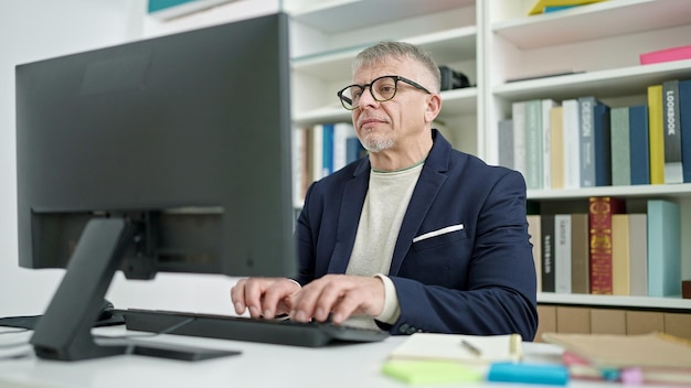 Middle age greyhaired man teacher using computer studying at university classroom