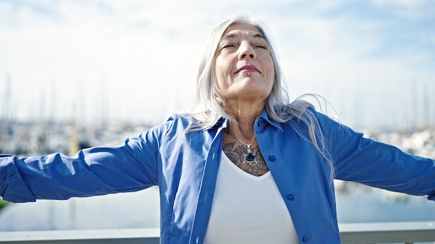 Middle age greyhaired woman breathing with arms open at seaside