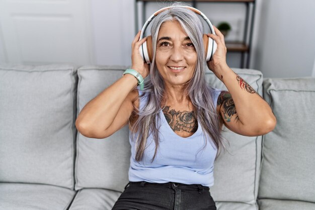 Middle age greyhaired woman smiling confident listening to music at home