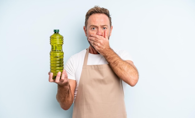 Middle age handsome man covering mouth with hands with a shocked olive oil concept