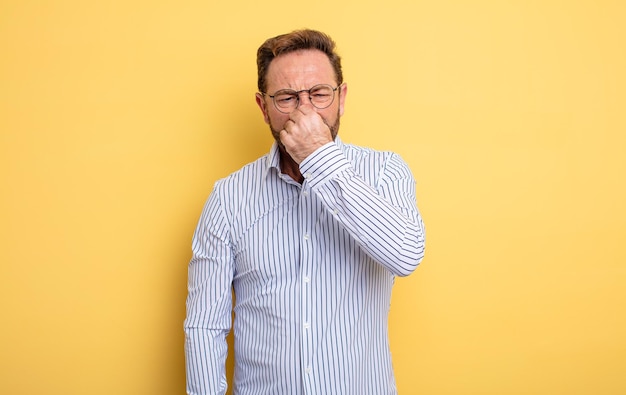 Middle age handsome man feeling disgusted, holding nose to avoid smelling a foul and unpleasant stench