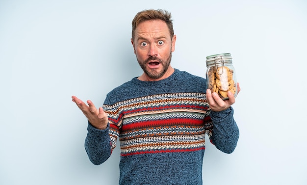 Middle age handsome man feeling extremely shocked and surprised. cookies bottle