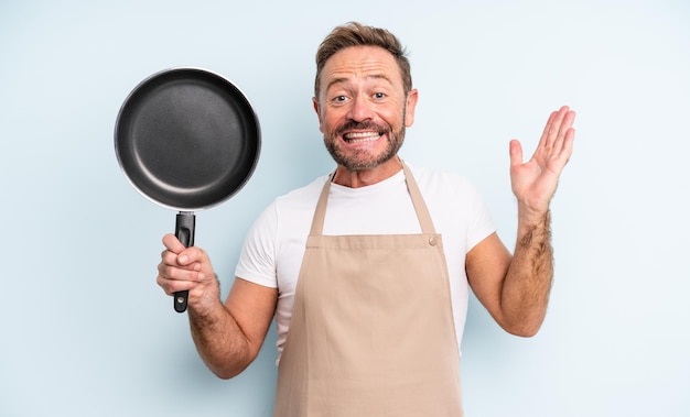 Middle age handsome man feeling happy and astonished at something unbelievable. frying pan concept