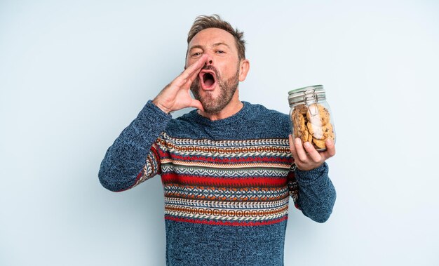 Foto uomo bello di mezza età che si sente felice, dando un grande grido con le mani vicino alla bocca. bottiglia di biscotti