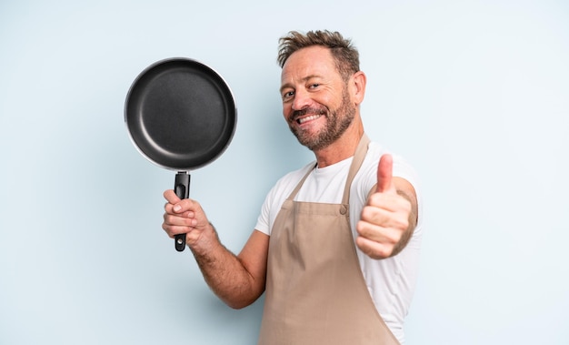 Middle age handsome man feeling proud,smiling positively with thumbs up. frying pan concept