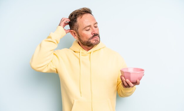 Middle age handsome man feeling puzzled and confused, scratching head. empty bowl concept