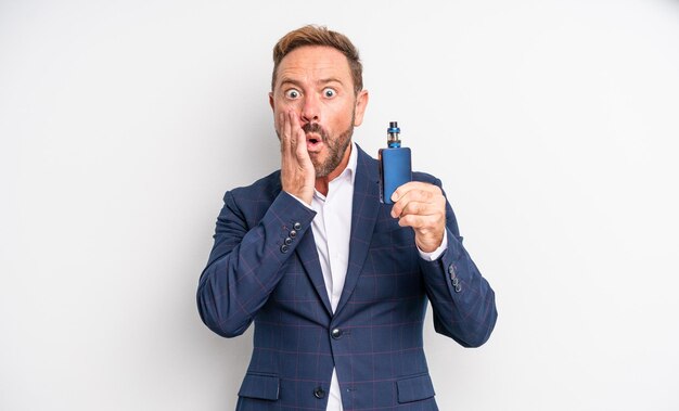 Middle age handsome man feeling shocked and scared smoking vaporizer concept