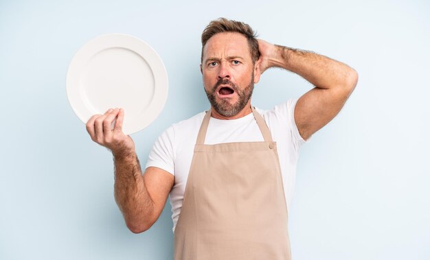 Middle age handsome man feeling stressed, anxious or scared, with hands on head. empty dish concept