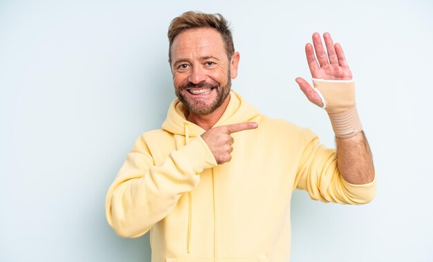 Middle age handsome man looking excited and surprised pointing to the side. broken hand concept