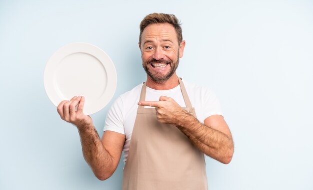 Foto uomo bello di mezza età che sembra eccitato e sorpreso che indica il lato. concetto di piatto vuoto