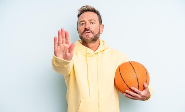 Middle age handsome man looking serious showing open palm making stop gesture. basketball concept