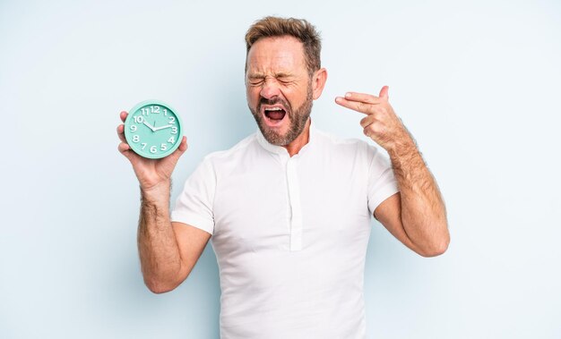 Middle age handsome man looking unhappy and stressed, suicide gesture making gun sign. alarm clock concept