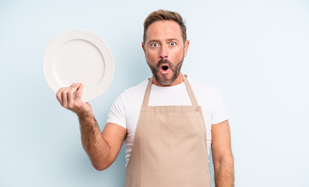 Middle age handsome man looking very shocked or surprised. empty dish concept