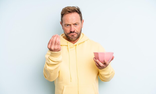Middle age handsome man making capice or money gesture, telling you to pay. empty bowl concept